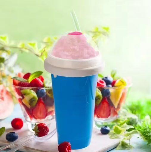 Blue slushy maker cup with pink slushie and straw, surrounded by fruit bowls on a light green background