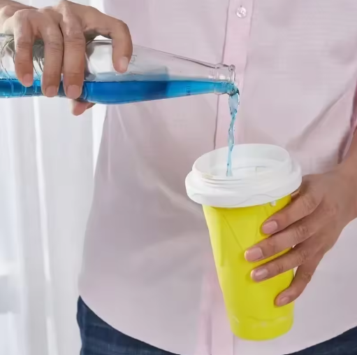 Person pouring blue liquid from a bottle into a yellow slushy maker cup with a white lid.
